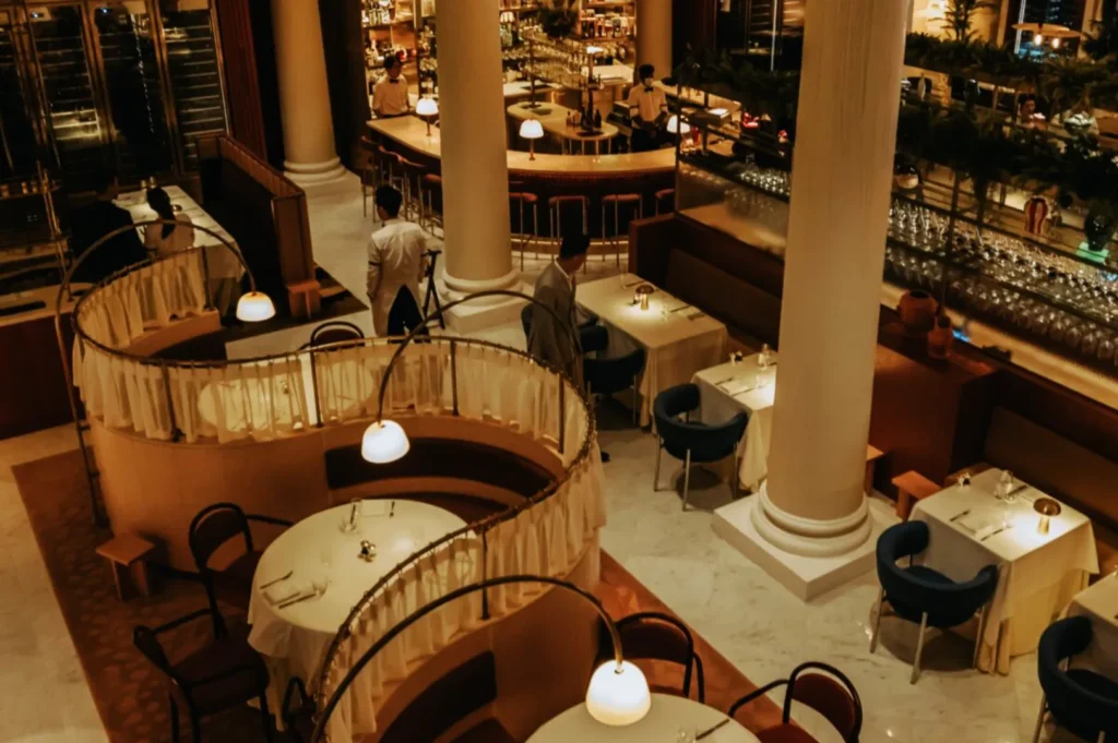 Elegant restaurant interior with plush, semi-circular booths and round tables set for dining. Warm lighting creates a cozy, inviting atmosphere.