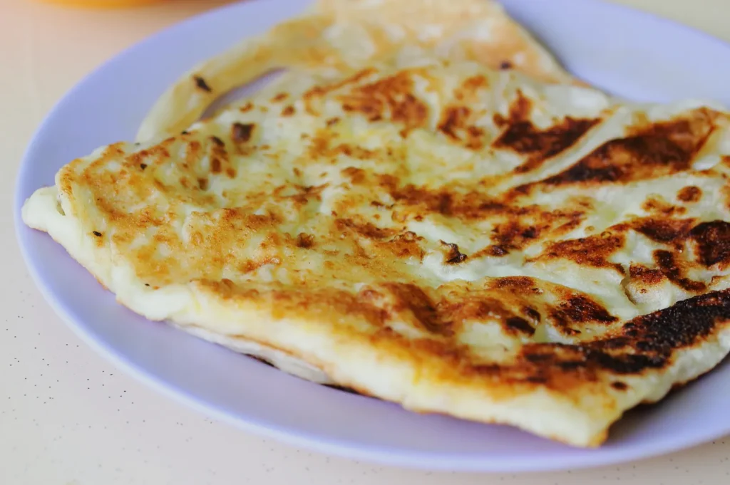 Golden-brown flatbread on a purple plate, showcasing crispy texture with charred spots, suggesting a freshly cooked, savory meal.