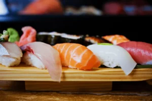 A wooden platter showcases an assortment of fresh sushi, including salmon, tuna, and eel, arranged neatly. The sushi conveys a sense of elegance and culinary delight.